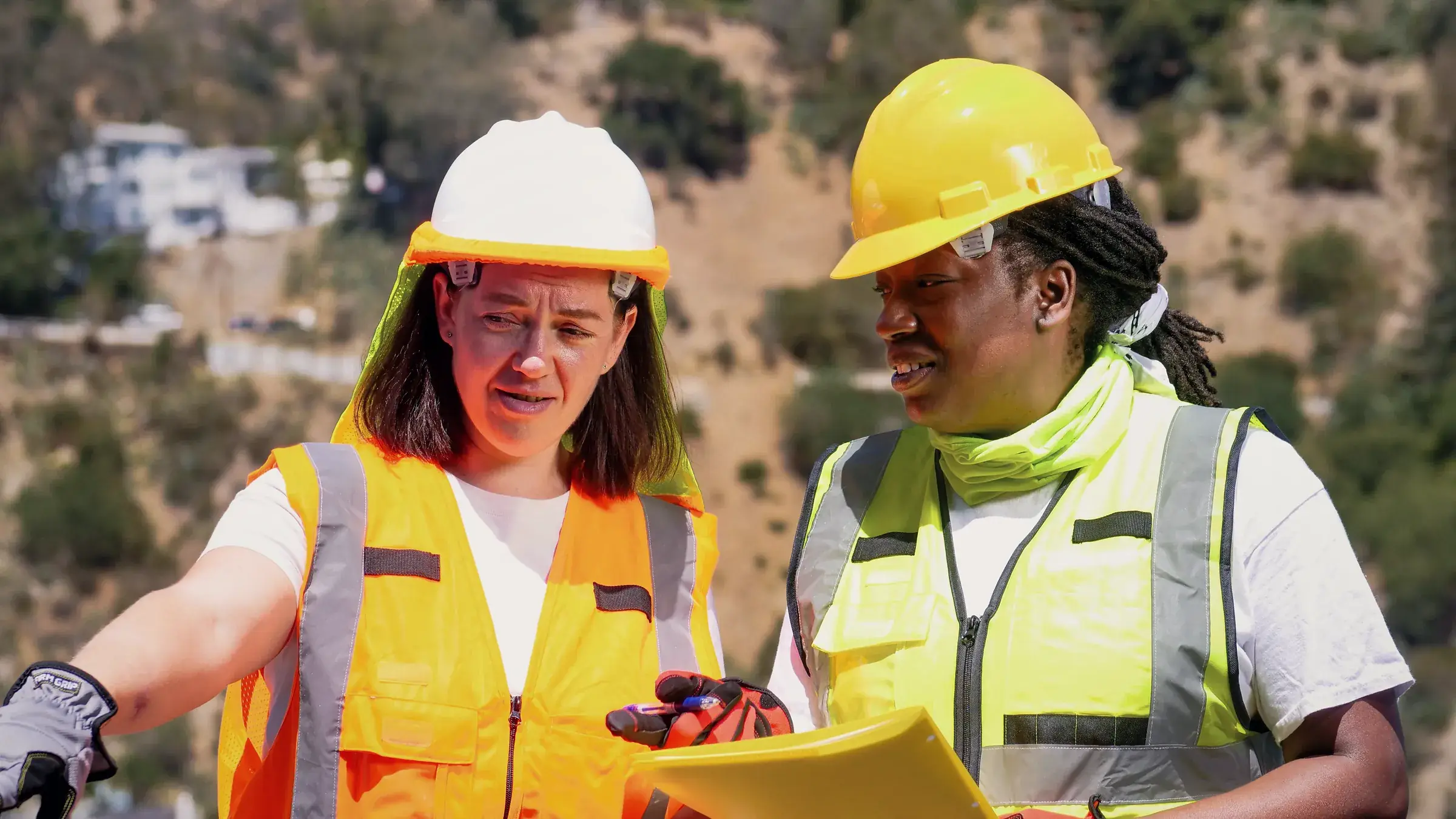 Two engineers in hard hats and high-visibility vests talking over a plan on site