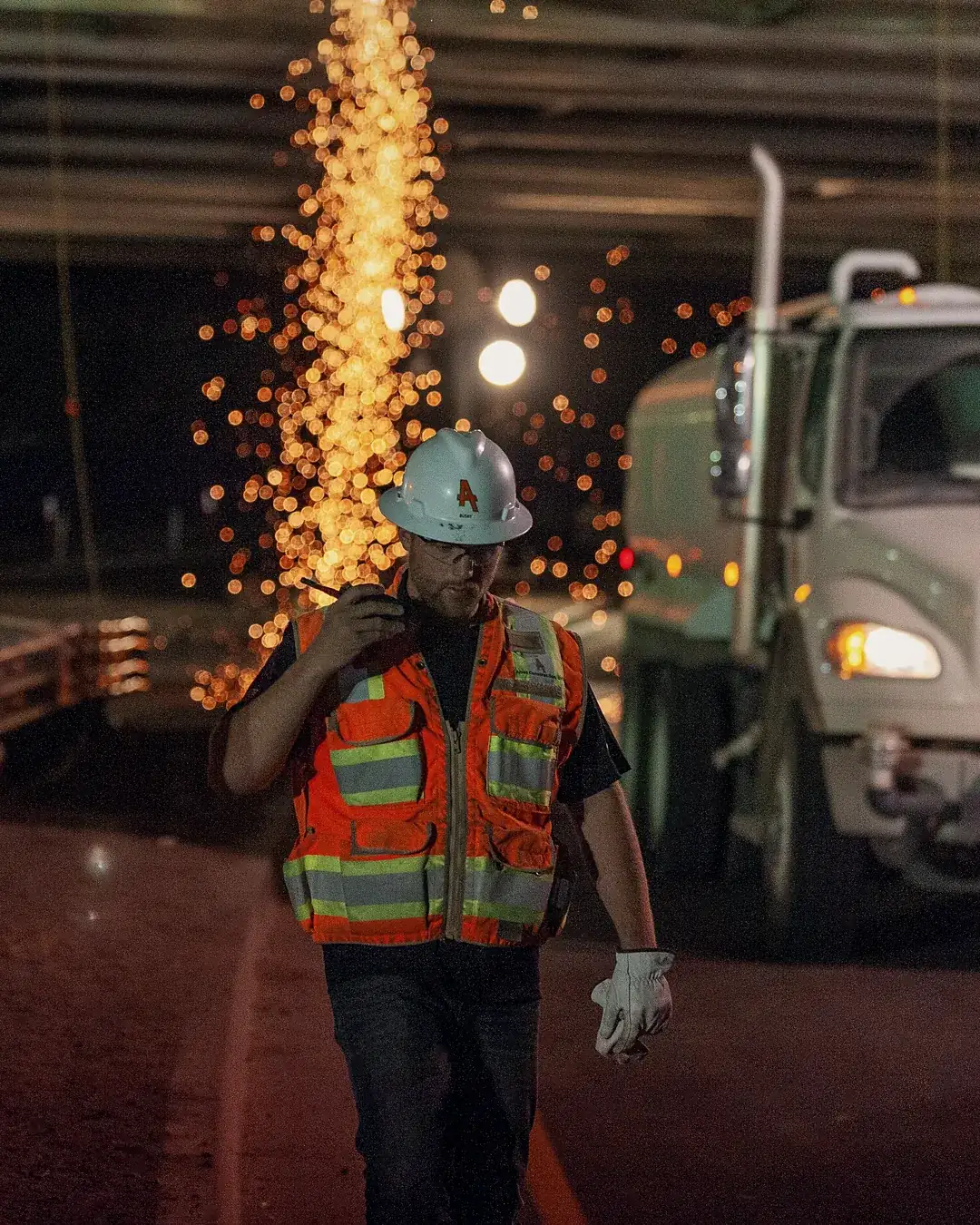 A night road crew in hard hats and high-visibility vests under an overpass, a truck behind them