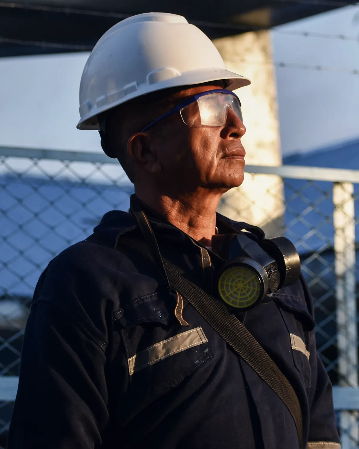 A plant worker in a hard hat, safety glasses and a respirator, outside the plant